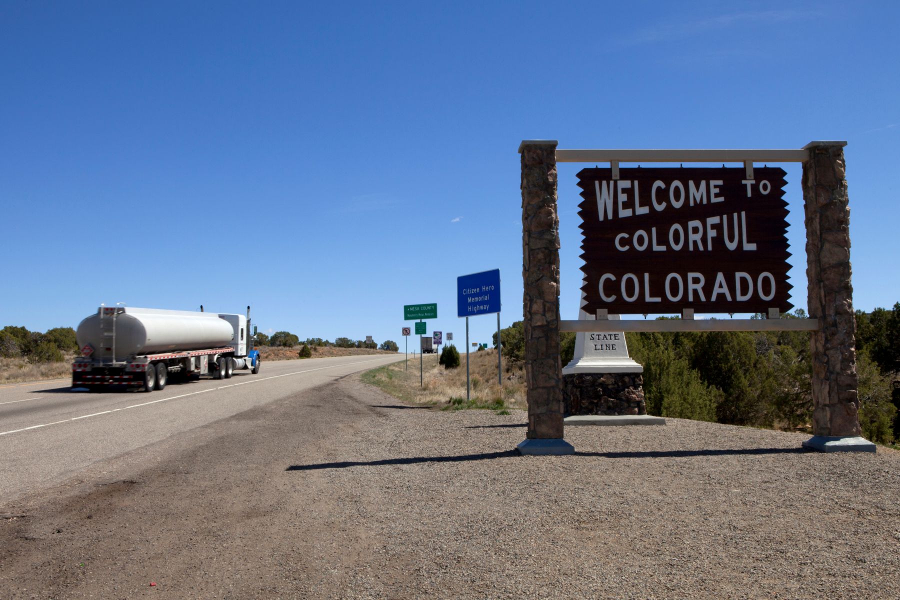 welcome-to-colorado-state-line-road-sign Roadside sign reading “Welcome to Colorful Colorado” at the state line along a highway, with a truck driving past under a clear blue sky.